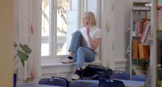 a woman sitting on the window sill in front of a book shelf