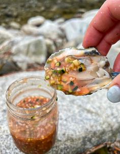 a person holding a spoon with some food on top of it next to a jar