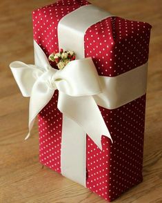 a red and white gift box with a bow on the top sitting on a wooden table