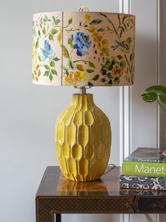 a yellow vase sitting on top of a wooden table next to a book and lamp