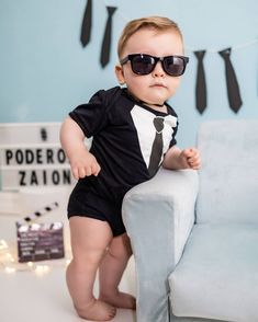 a little boy wearing sunglasses and a suit on top of a blue couch in front of a wall