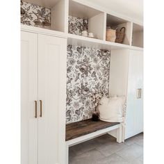 a room with white cupboards and floral wallpaper on the walls next to a bench