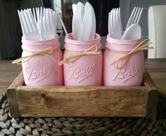 four pink mason jars with white forks and spoons in them sitting on a basket