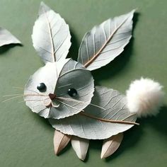 an animal made out of leaves on a green surface with white pom - poms