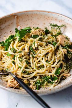 a white bowl filled with pasta and greens on top of a marble table next to a black fork