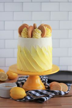 a yellow cake with white frosting and cookies on top sitting on a table next to lemons