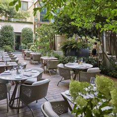 an outdoor dining area with tables and chairs, surrounded by greenery in the background