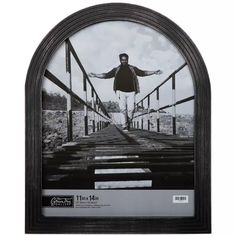 a black and white photo of a man standing on a bridge with his arms outstretched