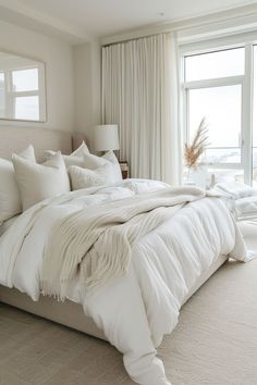 a bed with white linens and pillows in a bedroom next to a large window