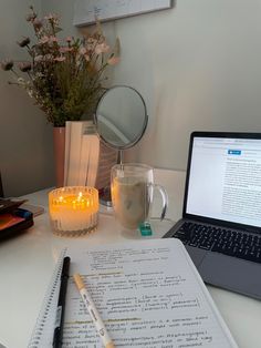 a laptop computer sitting on top of a white desk next to a cup and candle