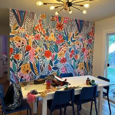 a dining room table with blue chairs in front of a colorful wall