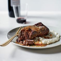 a white plate topped with meat and mashed potatoes next to a bottle of wine