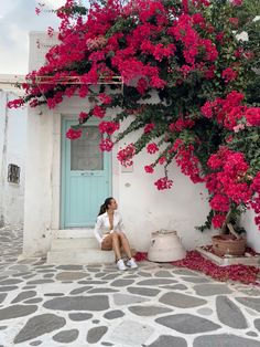 a woman sitting in front of a blue door with pink flowers on the outside wall