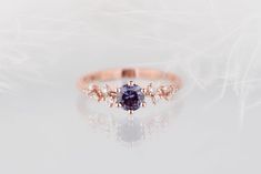 an engagement ring with a blue diamond surrounded by small white and pink diamonds on a reflective surface