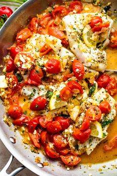 a pan filled with fish and tomatoes on top of a wooden table next to vegetables