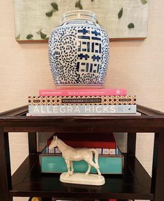 a horse figurine sitting on top of a table next to a vase and books