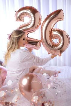 a woman sitting on top of a bed holding balloons in the shape of number twenty