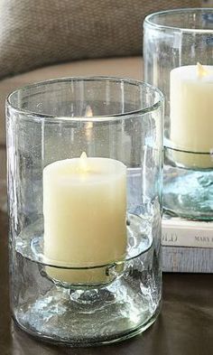 two clear glass candles sitting on top of a table next to a book and pillow