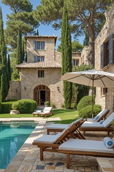 an outdoor pool with lounge chairs and umbrellas in front of the home's stone facade