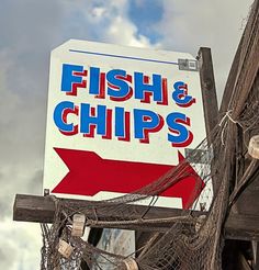 a fish and chips sign hanging off the side of a wooden pole in front of a cloudy sky