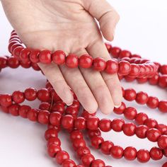 a hand reaching for red beads on a white surface