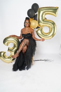 a woman in a black dress sitting on a chair with balloons and the number 55