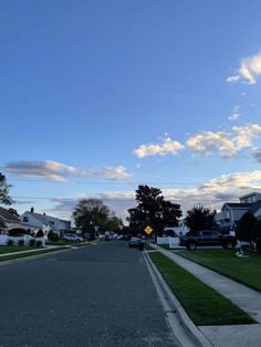 an empty street with houses and cars on the other side, in front of a blue sky