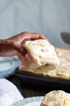 a person holding a piece of cinnamon roll with icing over it on a plate