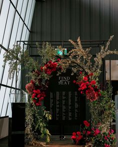 a floral display with red flowers and greenery on the wall in front of it