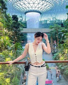 a woman in white pants and crop top standing on a balcony with palm trees behind her