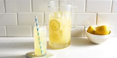 a pitcher of lemonade next to a bowl of lemons and a glass with a straw