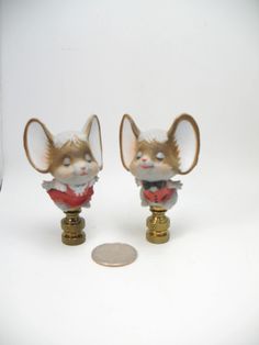 two small figurines sitting on top of each other next to a penny coin