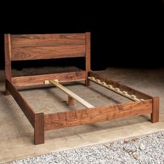 a wooden bed frame sitting on top of a cement floor next to a black wall