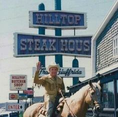 a man riding on the back of a brown horse next to a tall sign that says hilltop steak house