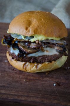 a close up of a hamburger on a wooden surface with cheese and meat in the middle