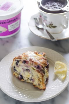 a muffin on a plate next to a cup of coffee and a lemon wedge