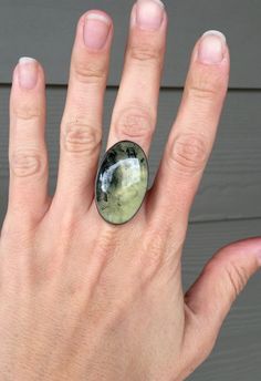 This stunning large oval apple green prehnite has been set in sterling silver with a handmade ring band from sterling silver half dome wire. The sterling silver has been given a dark patina or oxidized finish. Black flecks run through one side of this stone with white crystals throughout that catch the light and shine. This prehnite is 34mm x 20mm in size and 8mm in height. Size 7.5 but can be sized up to an 8. Minimalist Green Oval Jewelry, Green Oval Prehnite Rings, Prehnite Gemstone Ring Jewelry, Prehnite Ring Jewelry Gift, Prehnite Ring Suitable For Gift, Prehnite Ring Jewelry For Gifts, Nature-inspired Oval Jewelry With Polished Finish, Gift Prehnite Ring Jewelry, Round Green Prehnite Jewelry