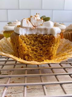 a cupcake with white frosting and sprinkles sits on a cooling rack