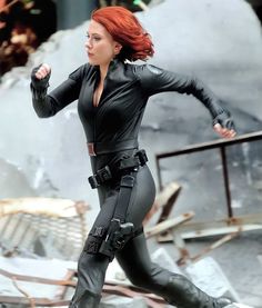 a woman with red hair is running on the street in black catsuits and boots