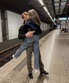 a man carrying a woman on his back at the train station while she is holding her