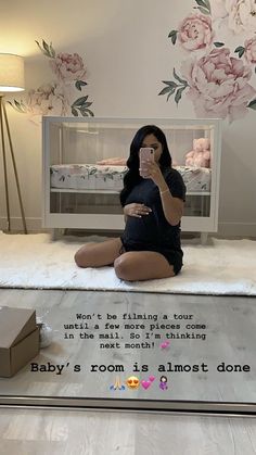 a woman taking a selfie in front of a baby's room with flowers on the wall