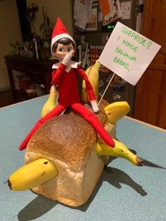 an elf is sitting on top of a banana bread sandwich, holding a sign that says surprise made banana bread