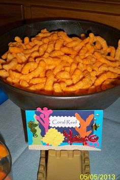 a bowl full of cheetos sitting on top of a table next to some candy