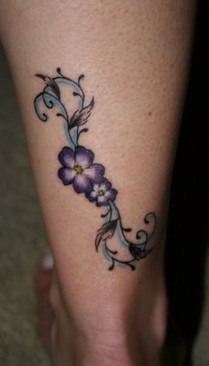 a tattoo on the leg of a woman with purple flowers and swirls around it