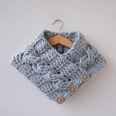 a crocheted scarf hanging from a hook on a white wall with a wooden hanger