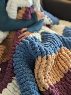 a woman sitting on top of a bed holding a baby in her arms and wearing a knitted blanket