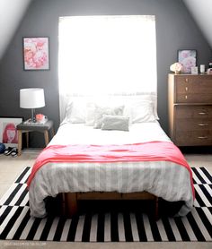 a white bed sitting under a window next to a black and white striped rug on top of a hard wood floor