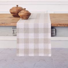 a table with two wooden bowls on it and a white checkered table cloth draped over the top