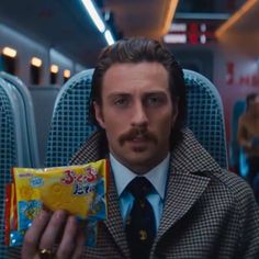 a man in a coat and tie is holding a bag of candy while sitting on an airplane