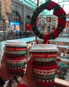 two people holding up coffee cups with christmas decorations on them in a shopping mall area